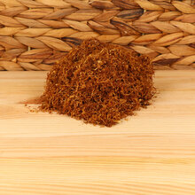 A small pile of fine cut Virginia tobacco on a plank of wood with wicker background